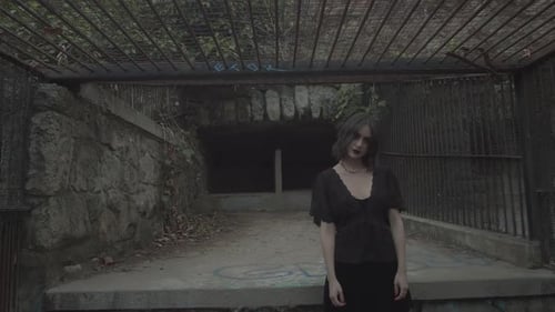 Creepy Pale Female With Dark Make Up And Black Dress Looking Spooky At The Camera While Turning Her