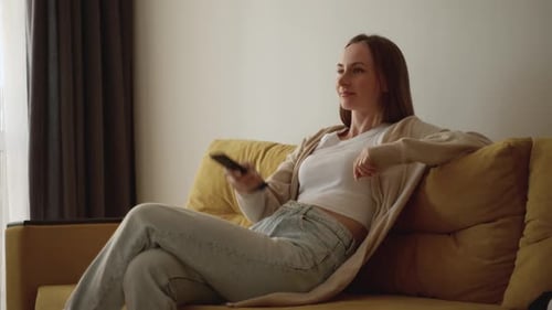 Woman Switches the Channel Using a Remote Control While Watching TV in Lifestyle at Home