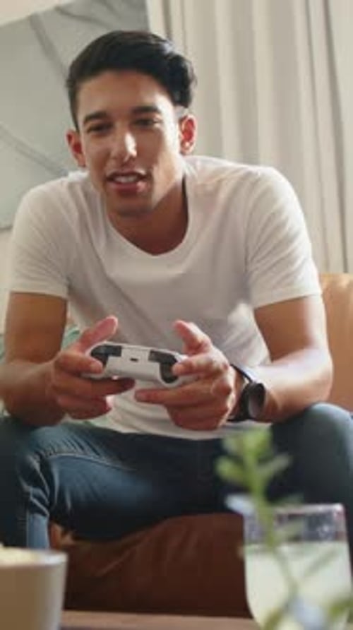 Vertical video: Playing man at game start with white controller on couch at home, grabbing drink