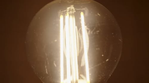 Nahaufnahme einer Glühbirne mit LED-Filamenten im Inneren, die langsam heller wird und blinkt.
