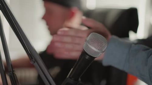 Nahaufnahme eines Mikrofons mit verschwommenem Hintergrund, das die Hand eines Mannes im Studio zeigt