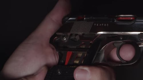 Hand holds pistol with exposed grip to see cartridge as hammer is pulled back