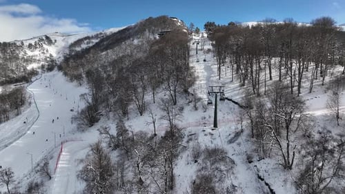 Drone footage of a modern cable car transporting tourists to the mountain peak over snowy ski trails