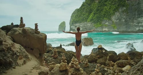 Woman By the Sea Traveler Girl in Swimsuit Admires the Rocky Ocean Landscape with Vibrant Turquoise