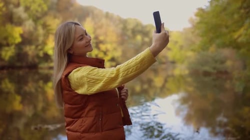 Young Woman Taking Selfie by Lake in Autumn Park