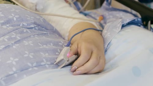 Pulse Oximeter Clipped On The Thumb Of A Covid Patient Lying On The Hospital Bed - close up