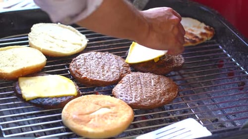 Putting cheese on patty on grill. Close up of beef patties on grill with cheese