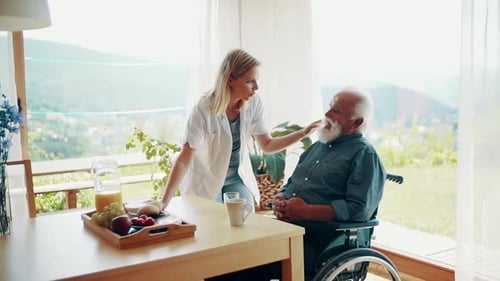 Woman Talking With Senior Man in Wheelchair Indoors