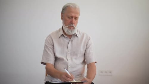 Studioporträt von Eleganz Nachdenklicher reifer Mann mit grauem Bart, der sich Notizen macht und aufschreibt