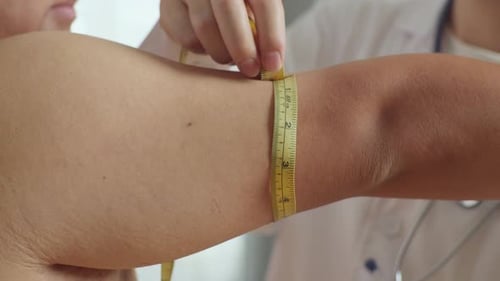 Close Up Of Male Doctor's Hands Using Tape Measuring Fat Male Patient's Arm