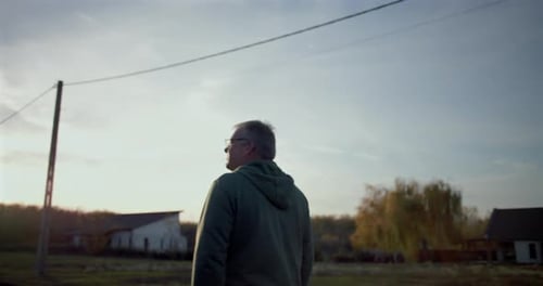 Man walking forward on a rural road, gazing ahead thoughtfully, serene open surroundings, utility