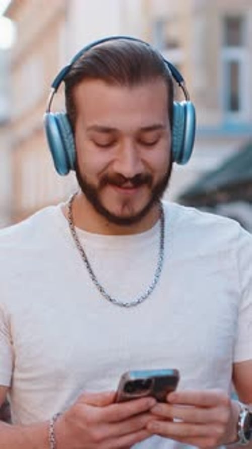 Happy Joyful Young Man in Wireless Headphones Choosing Listening Music Dancing Outdoors City Street