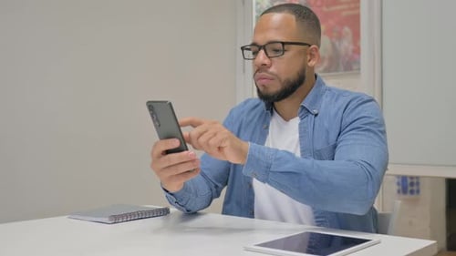 African Businessman Browsing Internet on Phone in Office