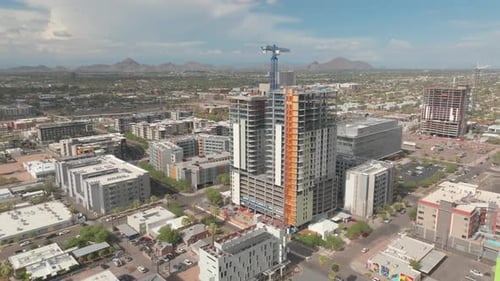 Rotating aerial footage of a hotel under construction with cityscape and mountains in the distance,