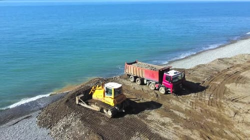Drone view of dump truck and bulldozer falling asleep on embankment by sea.