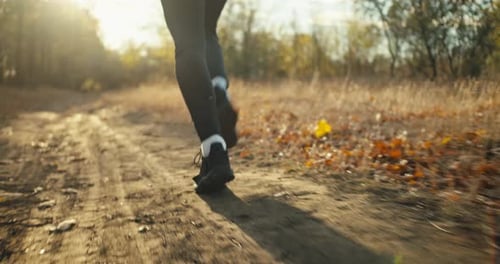 Close Up a Man in a Black Sports Uniform and Black Sneakers Runs Along an Earthen Path in the Autumn