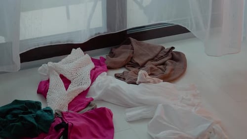 Messy clothes scattered on the floor near a window during afternoon light
