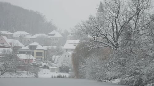 Snow blankets the trees and houses around a small pond in a peaceful Prague neighborhood.