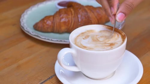 Stirring Coffee with a Croissant for Breakfast