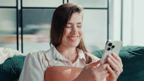 Smiling Woman Using Smartphone on Couch Indoors