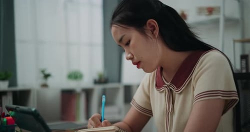 Woman Writes in Notebook While Studying at Desk