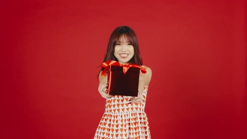 Smiling Woman Offers Gift on Red Background