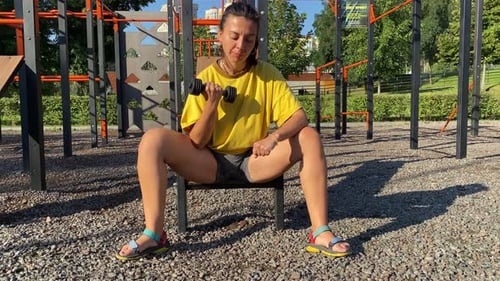 Multiracial Woman Energizing Bicep Workout in Outdoor Gym