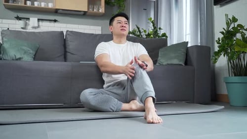 Man Massaging Knee Soreness Indoors on Exercise Mat