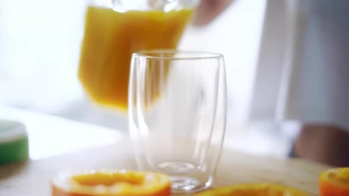 Woman Pouring Orange Juice From Glass Jar Into Glass. Close Up Glass Of Fresh Orange Juice. Prepa...