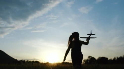 Selective focus of playful little girl kid run with an airplane on background sunset