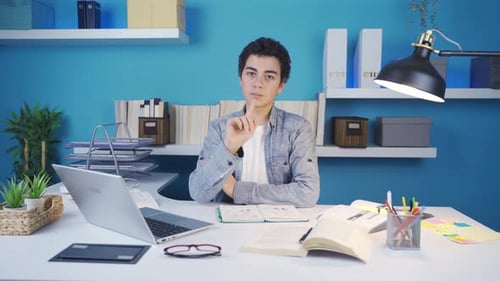 Young man looks at camera and makes a negative sign using his hand, nodding negatively.