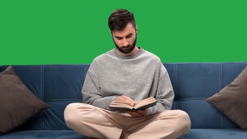 Concentrated Man Reading Interesting Paper Book Sitting on Couch at Home Chroma Key Green Screen