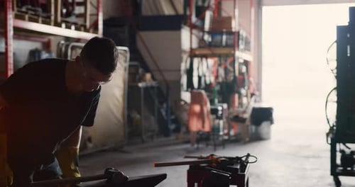 Professional blacksmith works hot metal at anvil in interior workshop