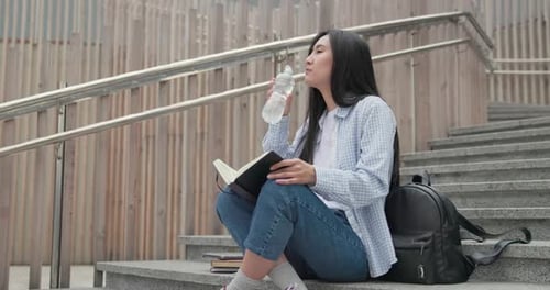 Woman Drinks Water While Studying on Steps