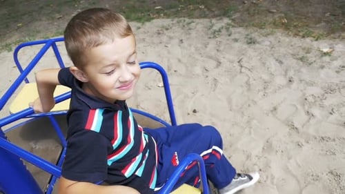 Niño feliz dando vueltas en el carrusel del patio de recreo en cámara lenta