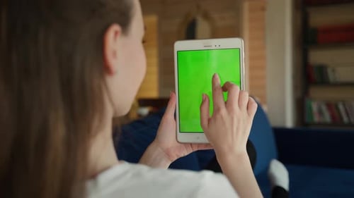 Rear View of a Woman Touching a Tablet with a Green Screen Sitting on a Blue Sofa in the House