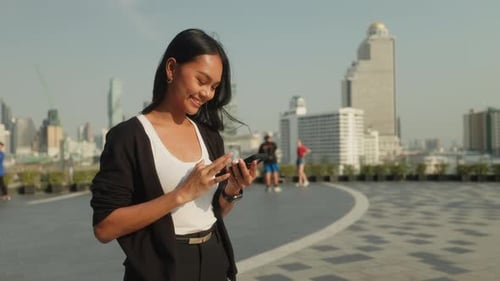 Portrait of Asian Businesswoman Browses Internet on Smartphone on City Square