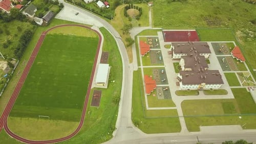 Aerial View of Sports Stadium with Red Running Tracks and Green Grass Football Field Near School