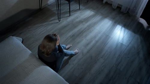 Blonde Woman Sitting on Floor Holding Head at Night