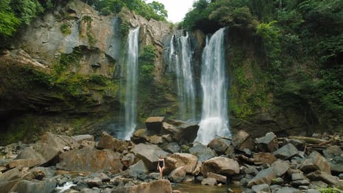 Woman exploring large waterfalls cascading over mossy rocks in a tropical forest