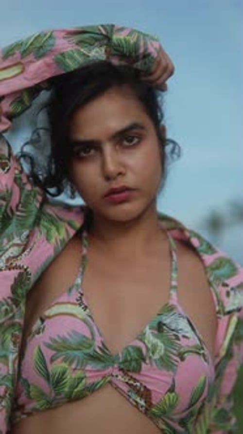 Confident woman with intense gaze outdoors wearing floral top against a blue sky background