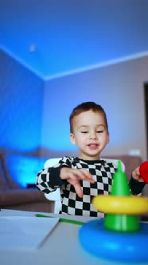 Adorable niño caucásico construyendo una pirámide sobre el escritorio. Lindo niño que aprende colores y tamaños en casa.