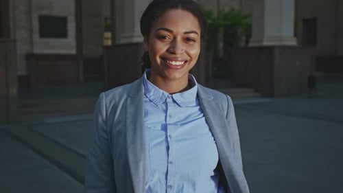 Smiling Woman in City Looks at Camera