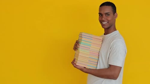 Smiling Student Boy Holding Academic Books Over Yellow Studio Background