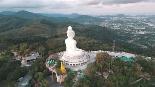 Aerial panning view of the Big Buddha overlooking Phuket Town illuminated by the setting sun.