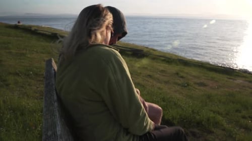 Adult couple sitting on bench and looking sunset with romance feeling, side view