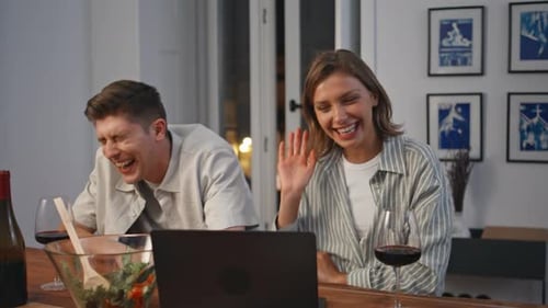 Cheerful Couple Laughing at Laptop With Wine at Home