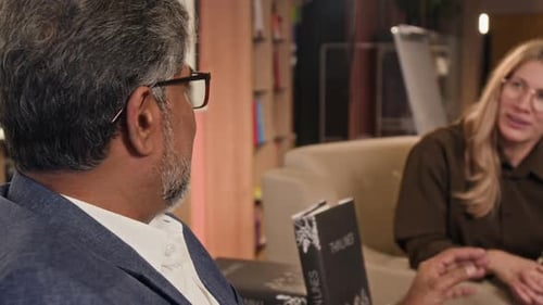 Man and Woman Sitting on Couch Discussing Book