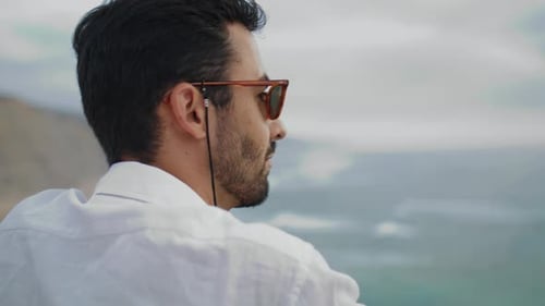 Man Overlooking Ocean From Cliff on Cloudy Day