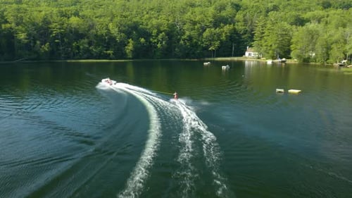 With numerous lush, green trees and few houses in the background, a woman in skis being carried by a